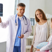 Mature doctor showing x-ray results to cute girl with her mother near by