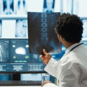 Physician reviewing MRI scan and x ray results with a patient in medical office, explaining the diagnostics. Doctor pointing at analysis to discuss about the illness, medical technology. Camera A.